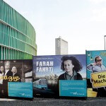 Plakate "High Voltage", "Good Guys", "Farah fährt" und "Die Macher" der VGF nebeneinander am Bauzaun